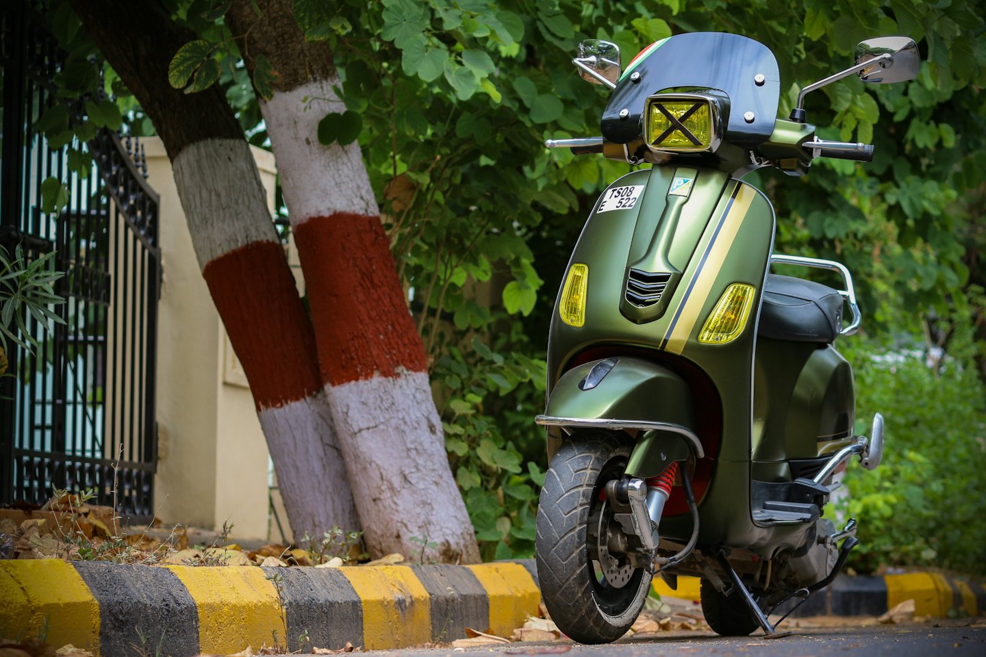 Scooter verde oliva retrò parcheggiata vicino a tronchi d'albero e marciapiede.